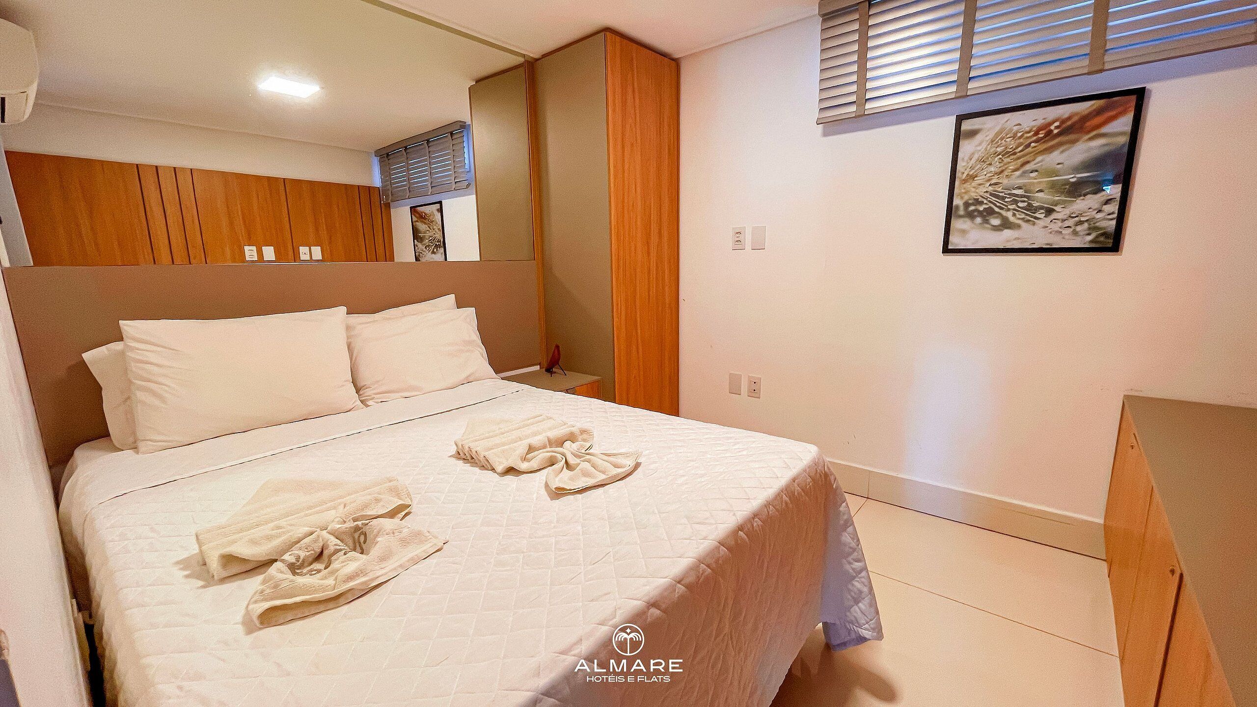 Una habitación de hotel con una cama, un armario de madera, una ventana con persianas y un cuadro en la pared.