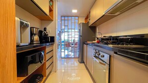 A narrow kitchen with modern appliances, a view through a glass door, and a logo for 'ALMARE HOTEL & FLATS'. - Solar Tambaú Luxo - By Almare Flats (João Pessoa)