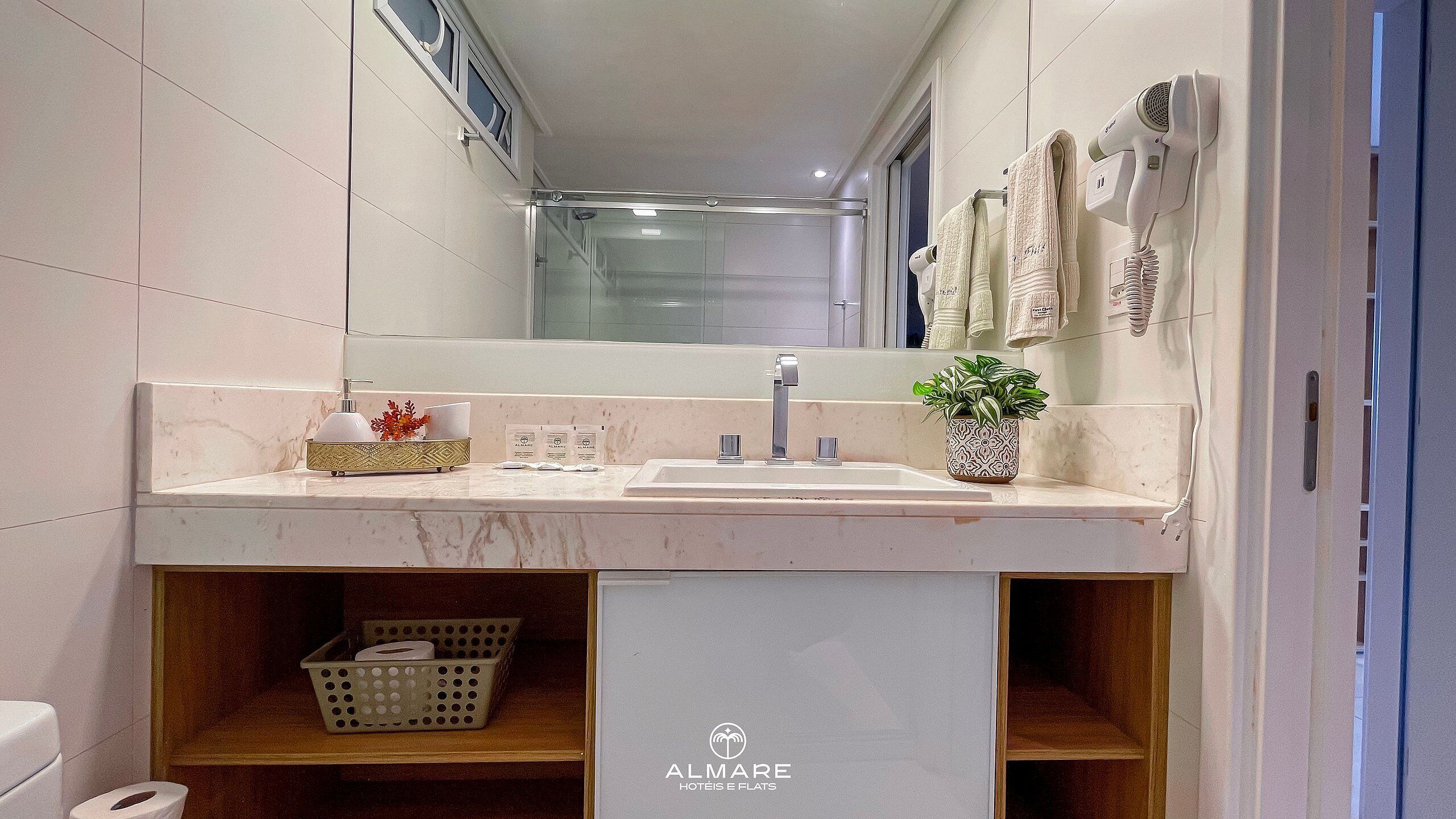 Un baño moderno con lavamanos de mármol, cabina de ducha con mampara de vidrio y un secador de pelo montado en la pared.