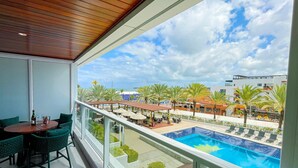 Un balcon avec vue sur une piscine, un espace salon extérieur et des palmiers.