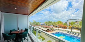 A balcony with a view of a swimming pool, outdoor seating, and palm trees. - Solar Tambaú Luxo - By Almare Flats (João Pessoa)