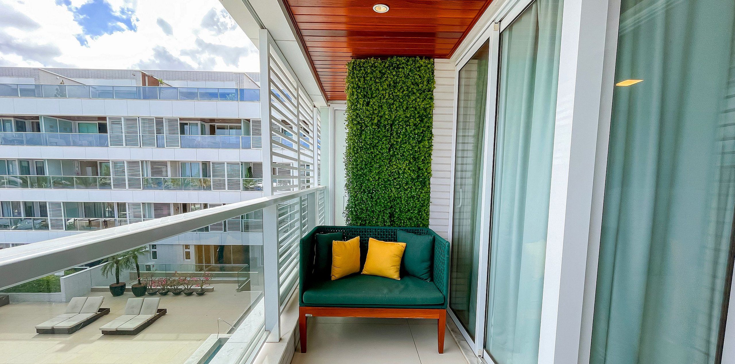 Un balcón con un sofá verde, un jardín vertical y vistas a un edificio moderno.