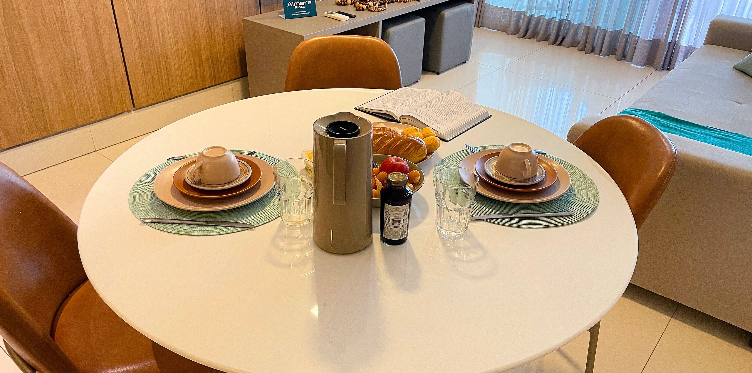 Una mesa de comedor dispuesta con dos tazas, un termo, una botella y un bol de fruta.