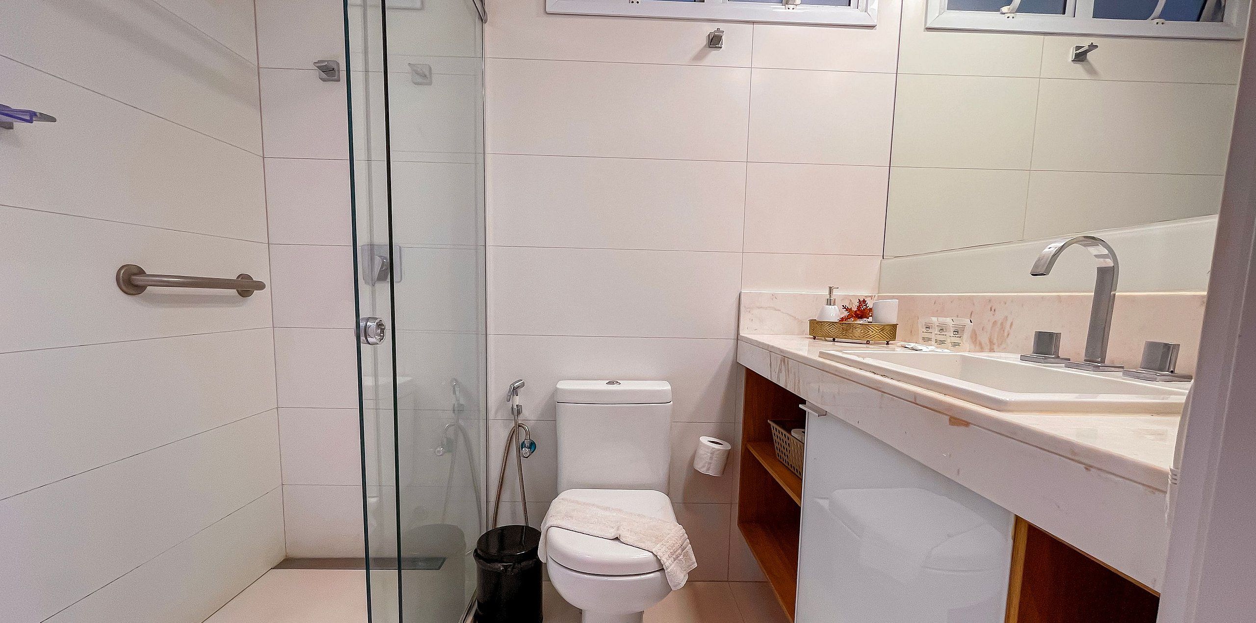 Un baño moderno con cabina de ducha de vidrio, inodoro, lavamanos con espejo y un cubo de basura.
