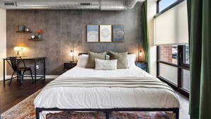 A modern bedroom with a large bed, a desk, and a chair. There are three framed artworks on the wall, and a window with curtains. - Eden Studio | Free Parking, Central, Gym Fast WIFI (Minneapolis)