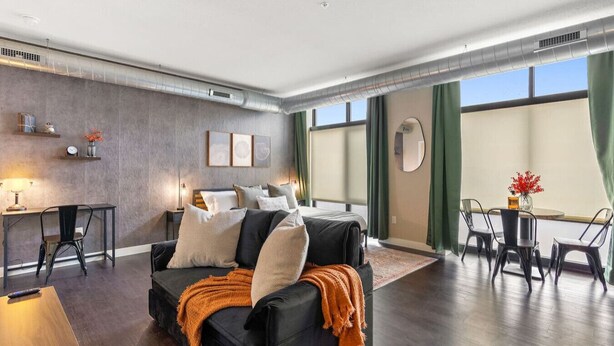 A modern hotel room with a large bed, a seating area with a table and chairs, and a view of the outdoors through large windows. - Eden Studio | Free Parking, Central, Gym Fast WIFI (Minneapolis)