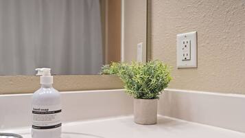 A bathroom with a white sink, a hand soap dispenser, and a small potted plant.