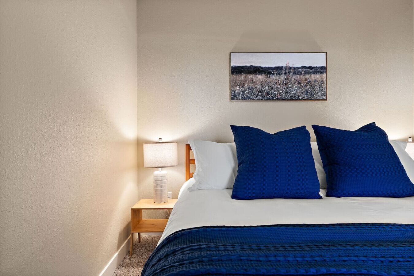 Una habitación de hotel con una cama, una mesita de noche con lámpara y un cuadro en la pared.
