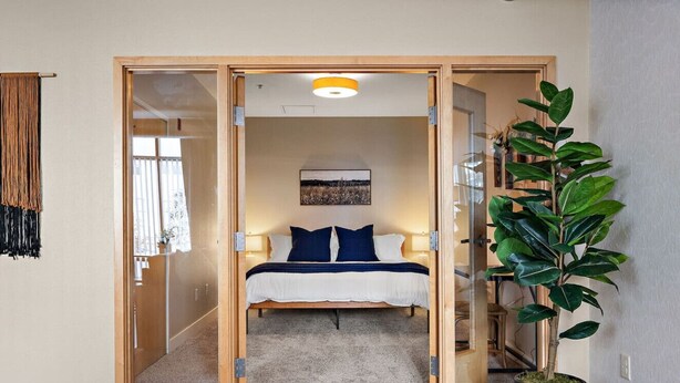 Een slaapkamer met een bed, een grote potplant en uitzicht buiten door een schuifdeur.