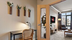 Hotelkamer met een bureau, stoel en een televisie in de zithoek. Er zijn wandplanters met bloemen en een grote spiegel.