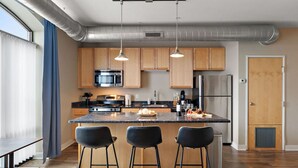 Een moderne keuken met houten kastjes, een centraal eiland met barkrukken, roestvrijstalen apparatuur en hanglampen.