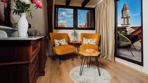 A room with a wooden floor, a white fluffy rug, two yellow chairs with floral cushions, a white vase with flowers, and a view of a building with a tower through a large window. - Villa Trogir Stars (Trogir)