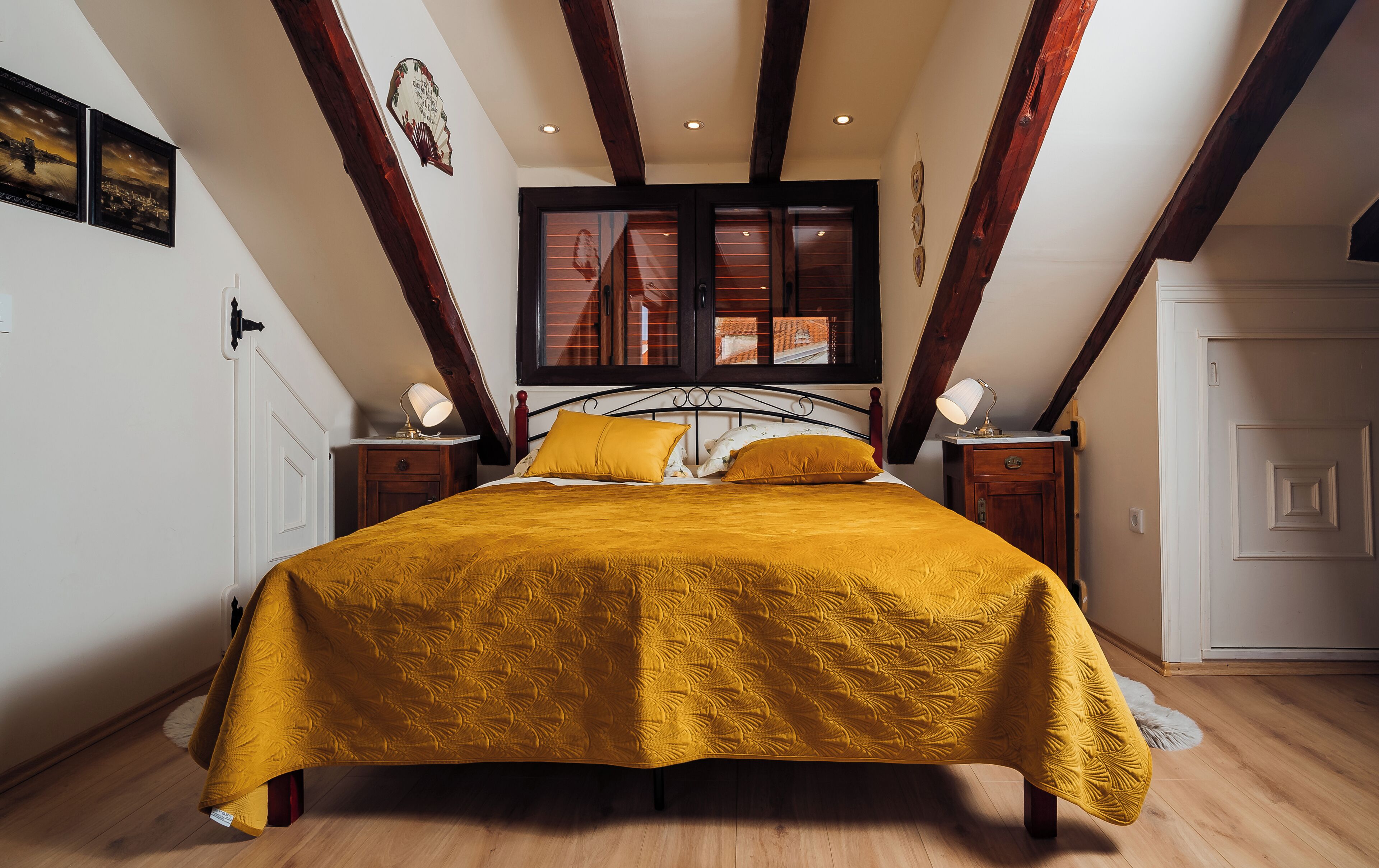 Un dormitorio con cama, vigas de madera, una ventana y una mesita de noche.