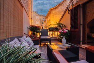 An outdoor seating area with wicker furniture, potted plants, and a view of the street.