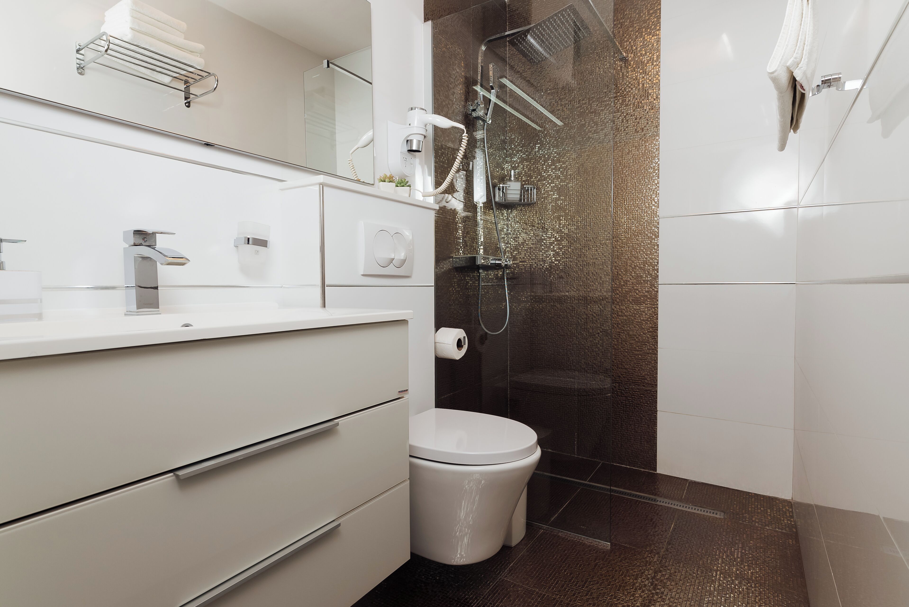 A modern bathroom with a white vanity, a toilet, a shower enclosure, and a towel rack.