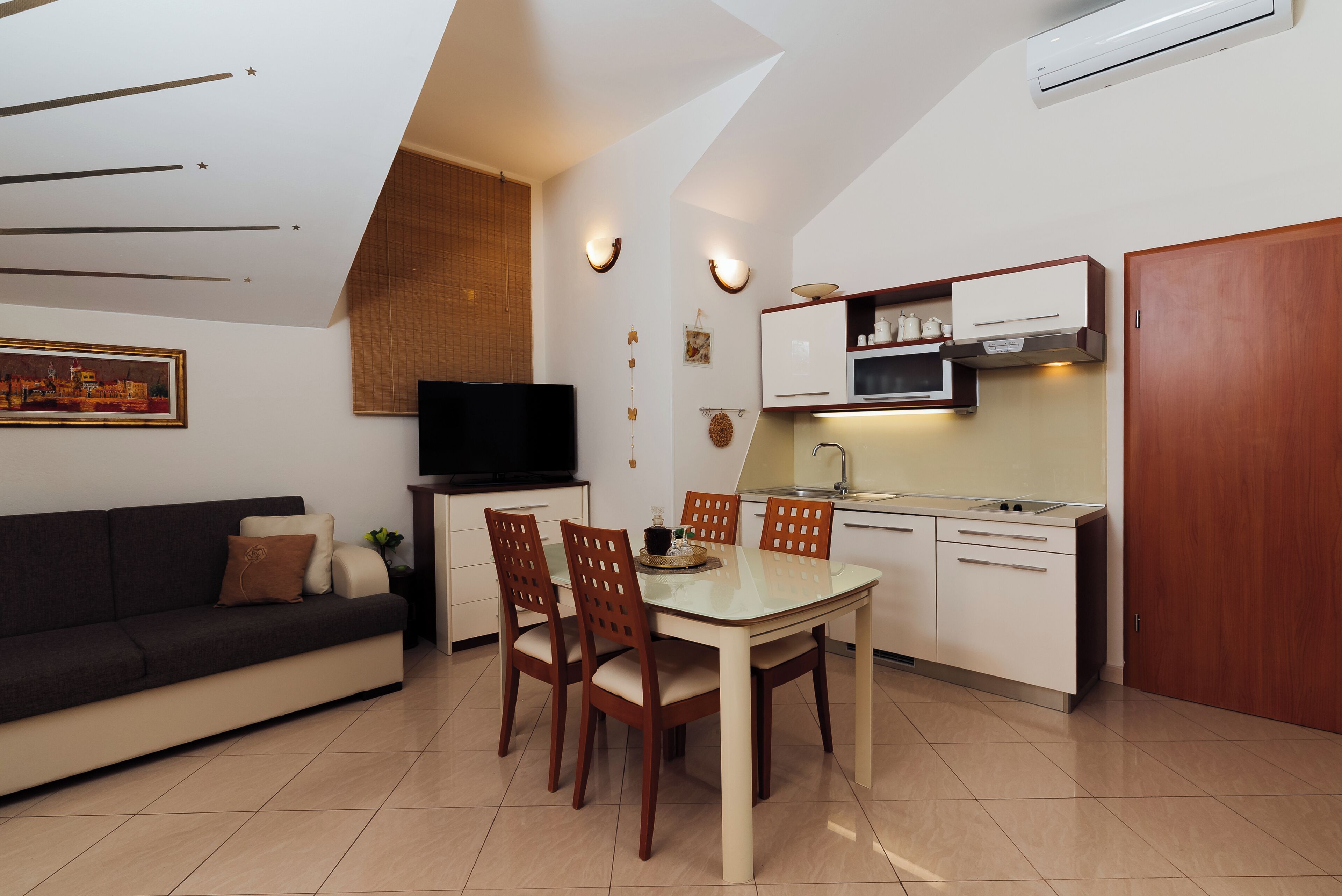 A modern kitchen with a dining area, a flat-screen TV, and a wooden door.