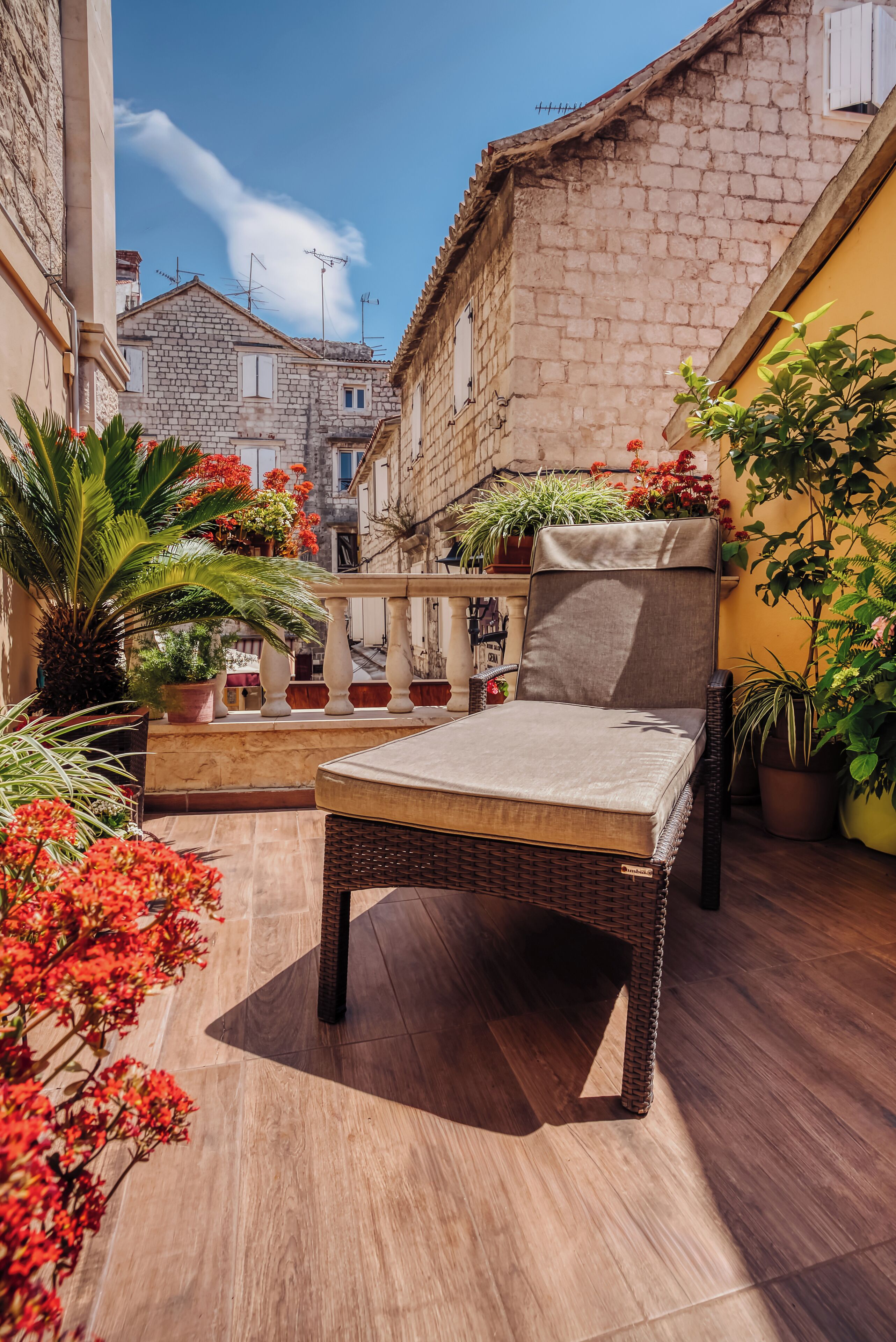A patio with a wicker chair and a table, surrounded by potted plants and flowers.