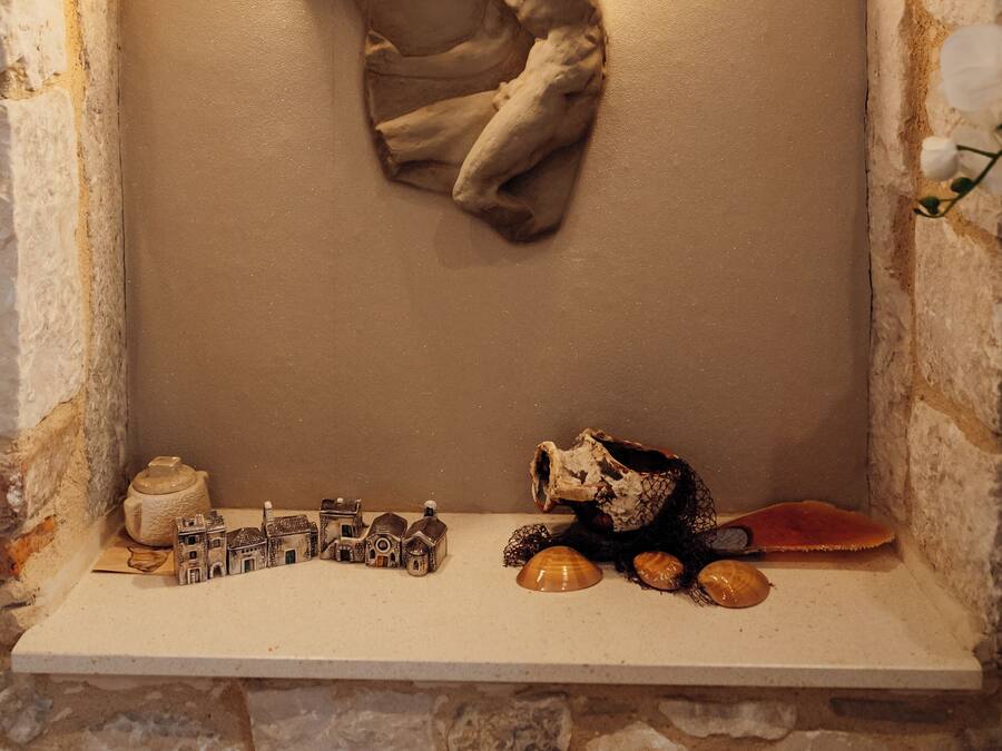 Um recanto com paredes de pedra, um tecido pendurado, uma prateleira com objetos decorativos e duas luzes fixadas na parede.
