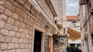 A narrow stone-paved alley with buildings on either side, featuring a stone wall, a wooden door, and a small outdoor seating area with umbrellas. - Villa Trogir Stars (Trogir)