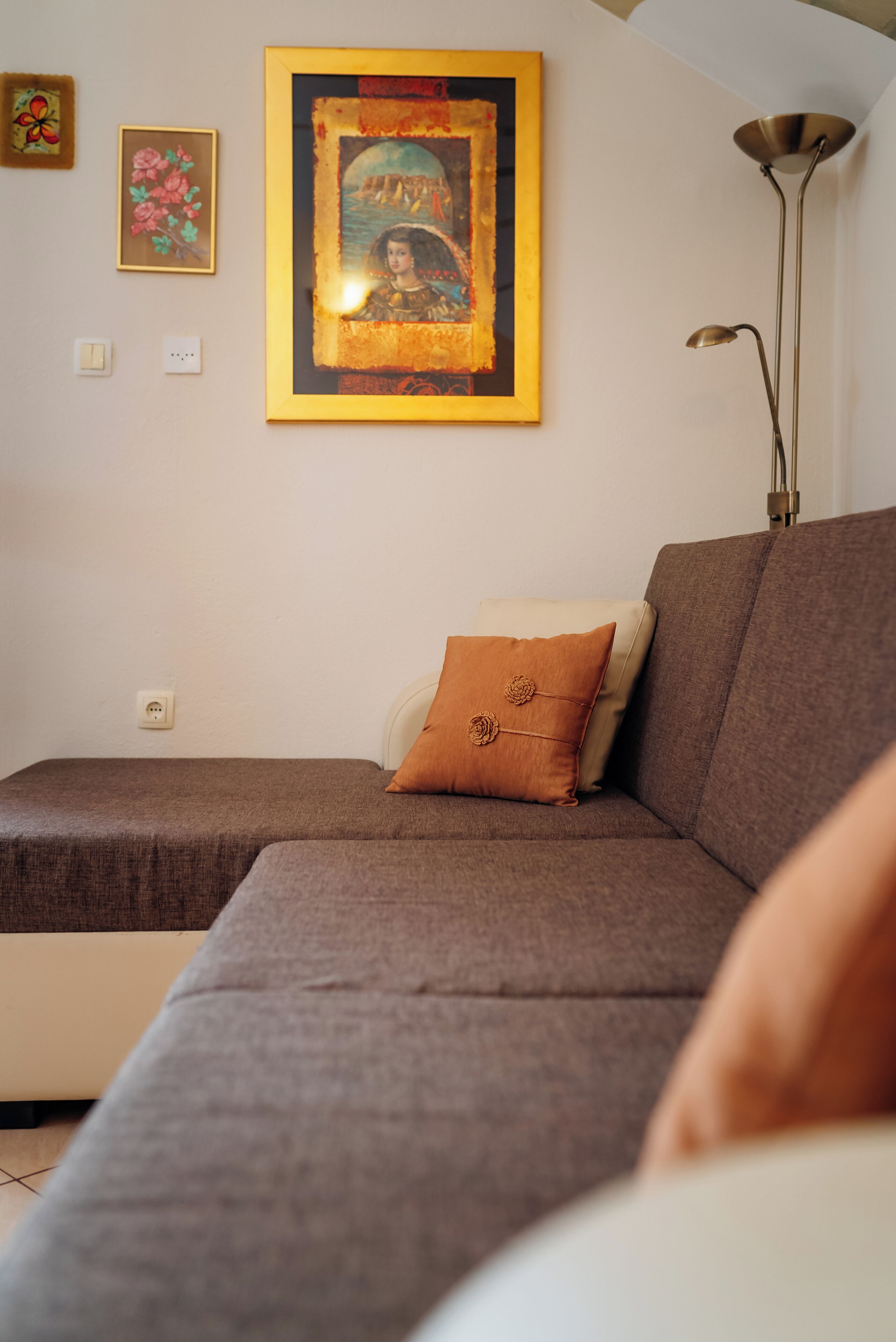 A living room with a brown sofa, a framed artwork on the wall, and a floor lamp.