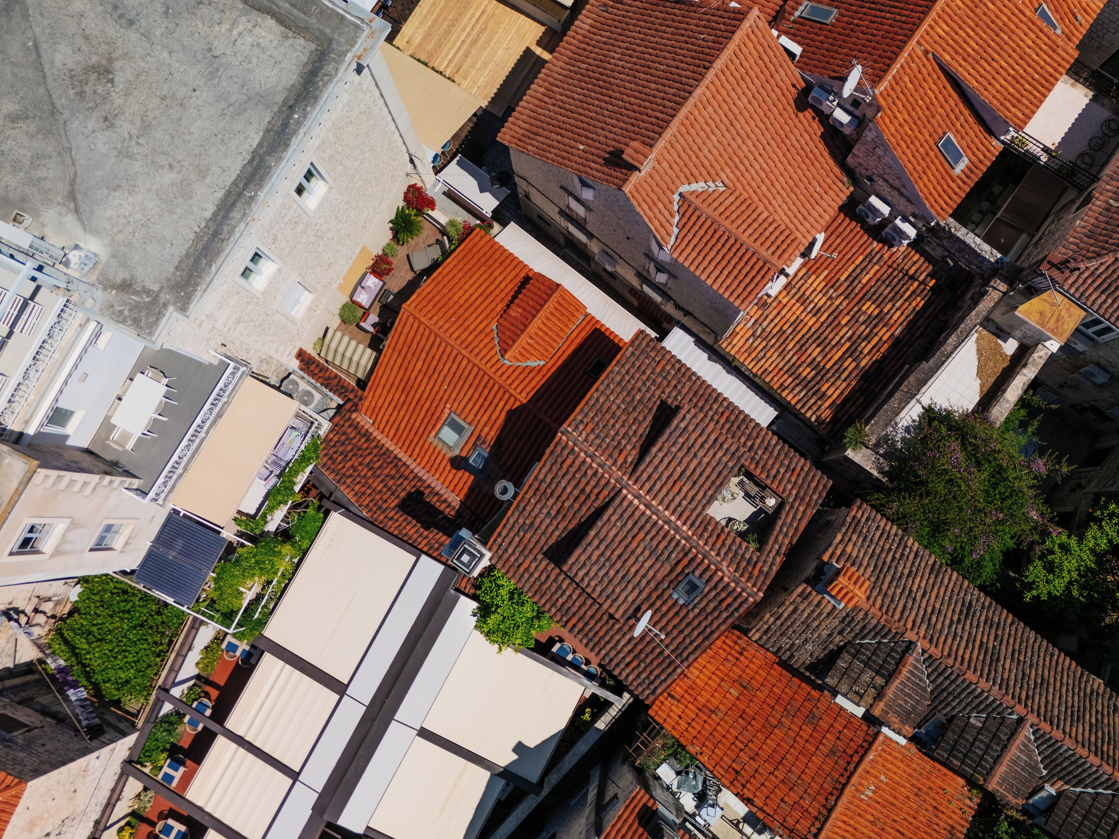 A high-angle view of a densely packed urban area with a mix of traditional and modern buildings, featuring a variety of roof styles and some greenery.