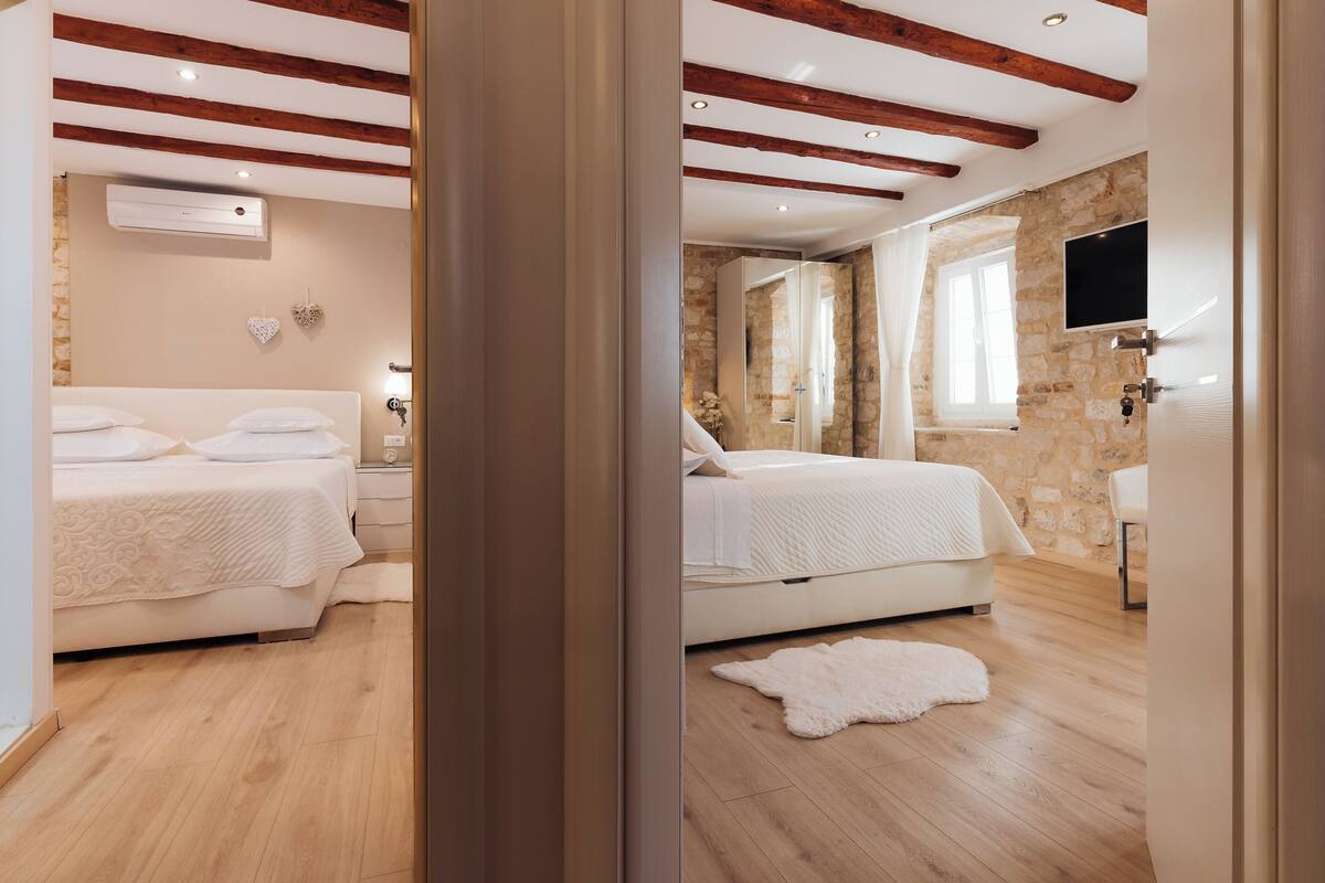 Ein Schlafzimmer mit zwei Betten, Holzbalken, Steinwänden, einem Flachbildfernseher und einem weißen, flauschigen Teppich.
