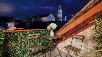 Un área de estar al aire libre con una mesa y sillas, un jarrón con flores y vistas a una torre de iglesia.