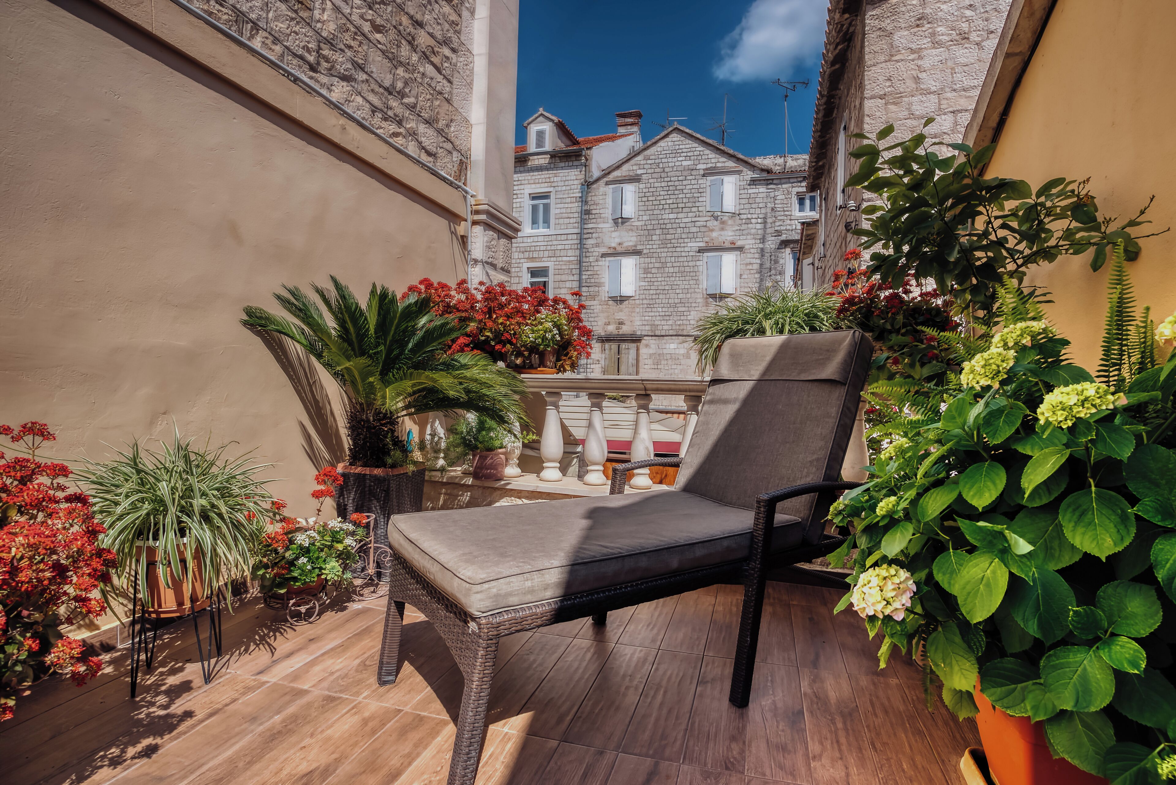 A balcony with a wicker chair, potted plants, and a view of a building with multiple windows.