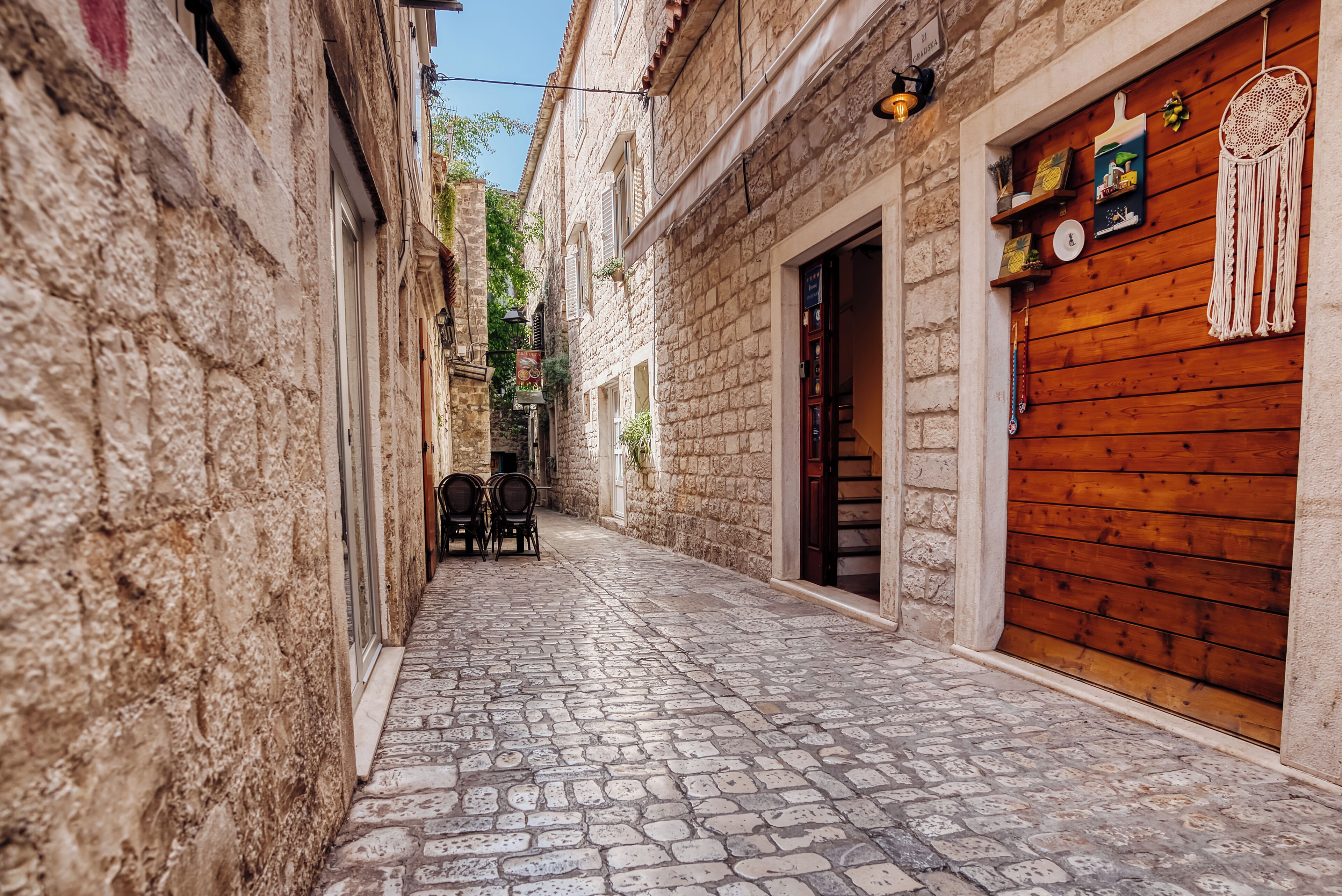 Une ruelle étroite pavée, bordée de bâtiments en pierre dotés de portes et de volets en bois.