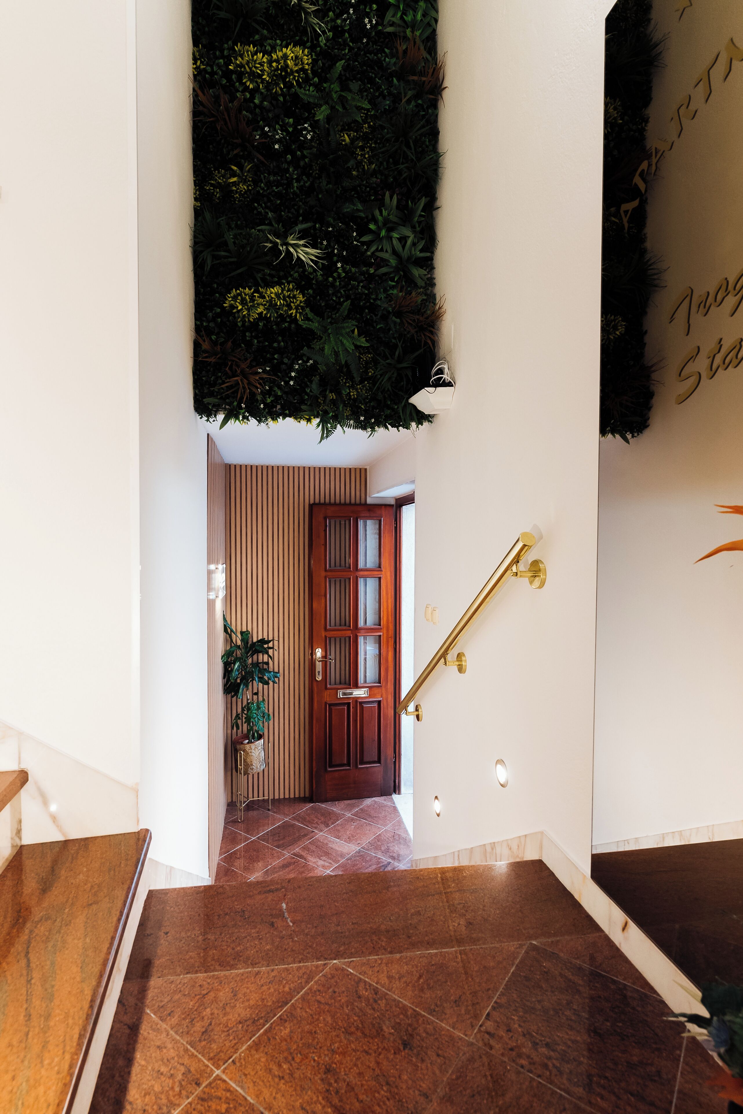 Una escalera con barandilla de madera, una planta en maceta y una puerta con paneles de vidrio.