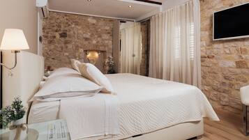 A bedroom with a stone wall, a bed with white bedding, a bedside lamp, and a flat-screen TV mounted on the wall.