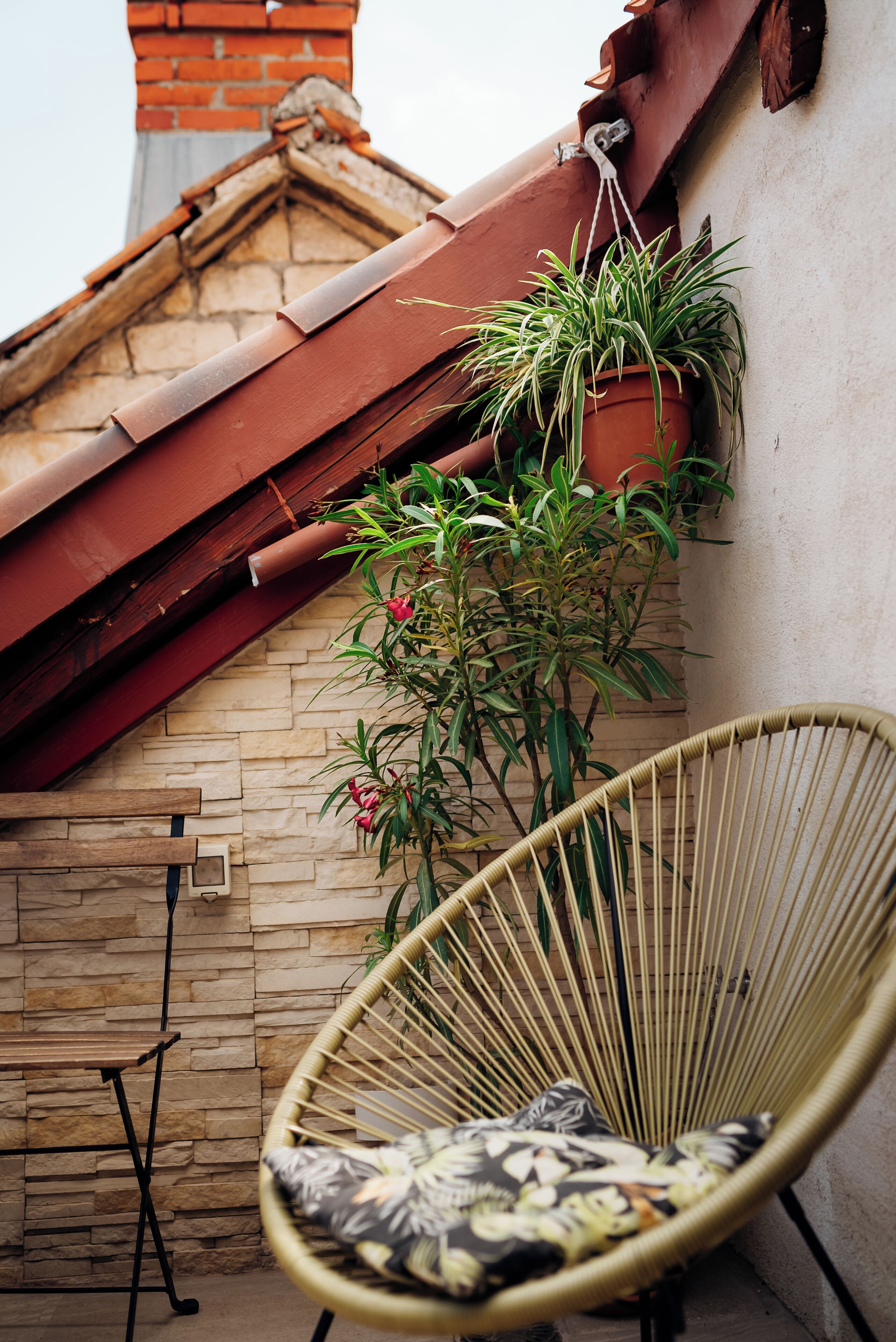 A wicker chair with a patterned cushion, a potted plant, and a brick wall with a tiled roof.