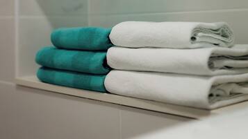 A bathroom with white tiled walls, a glass shelf with towels, and a white bathtub.