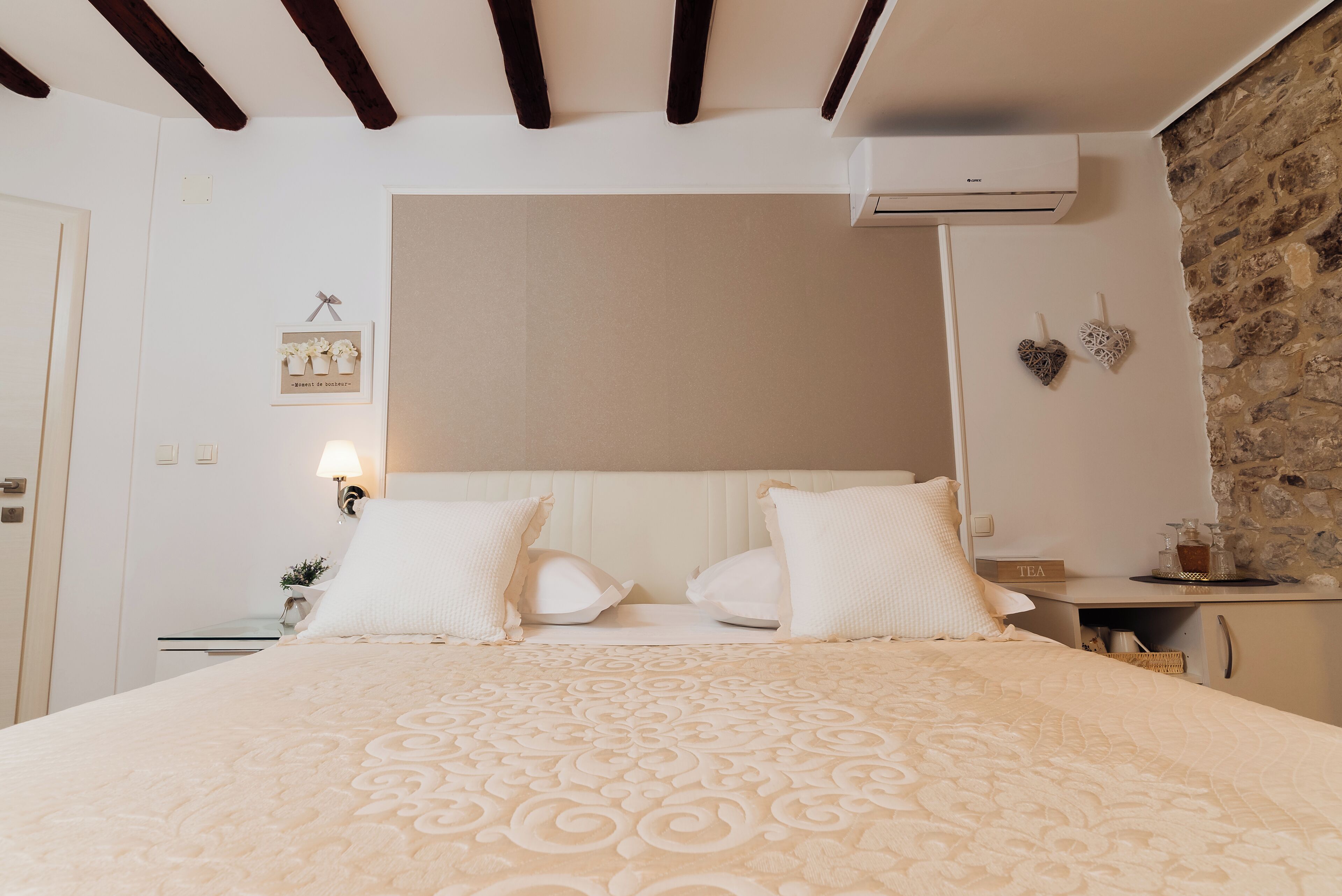 Un dormitorio ordenado con cama, mesitas de noche, aire acondicionado de pared y pared de piedra.