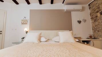 Un dormitorio ordenado con cama, mesitas de noche, aire acondicionado de pared y pared de piedra.