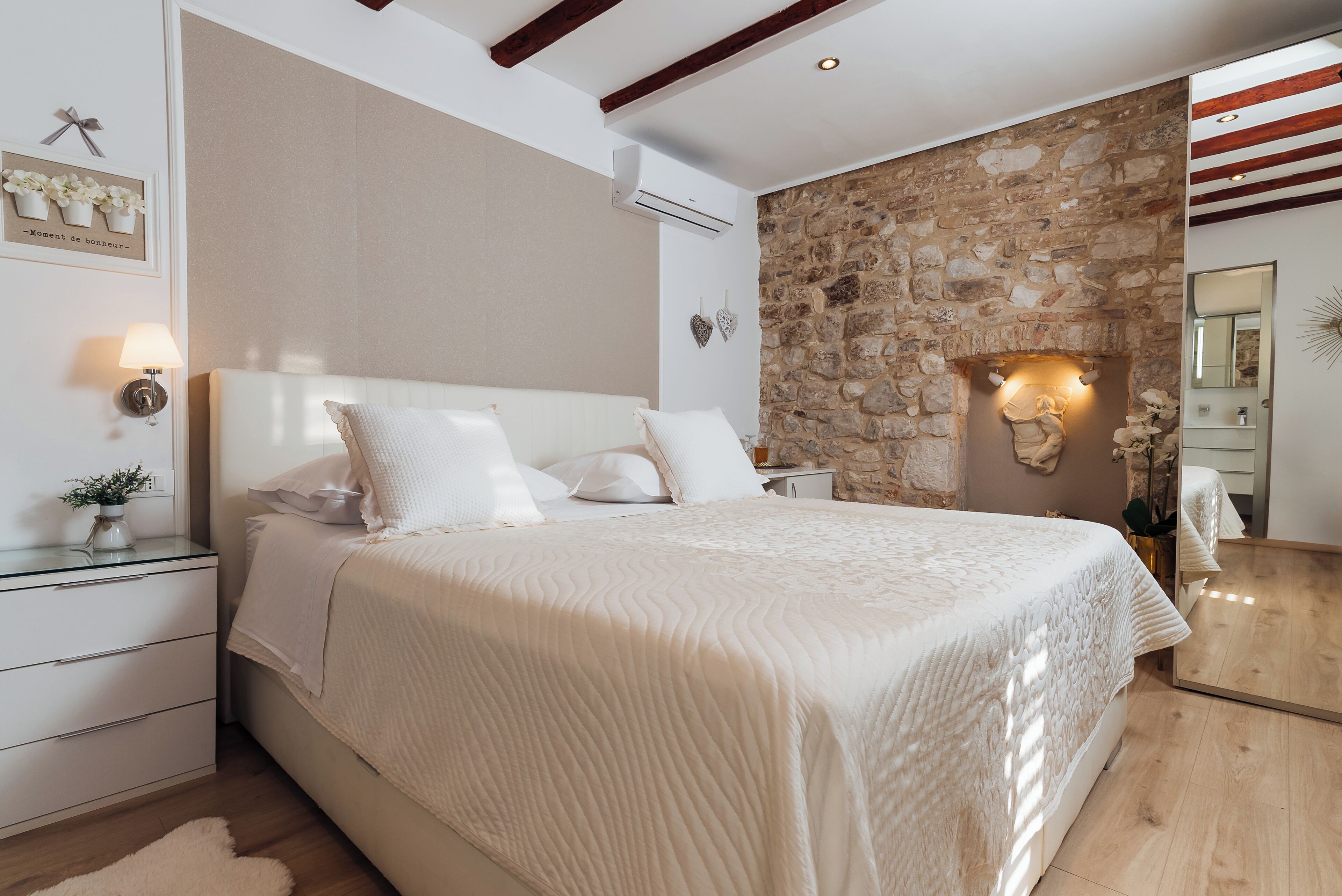 Una camera da letto con un letto grande, un muro in pietra, un soffitto in legno e un comodino con una lampada.