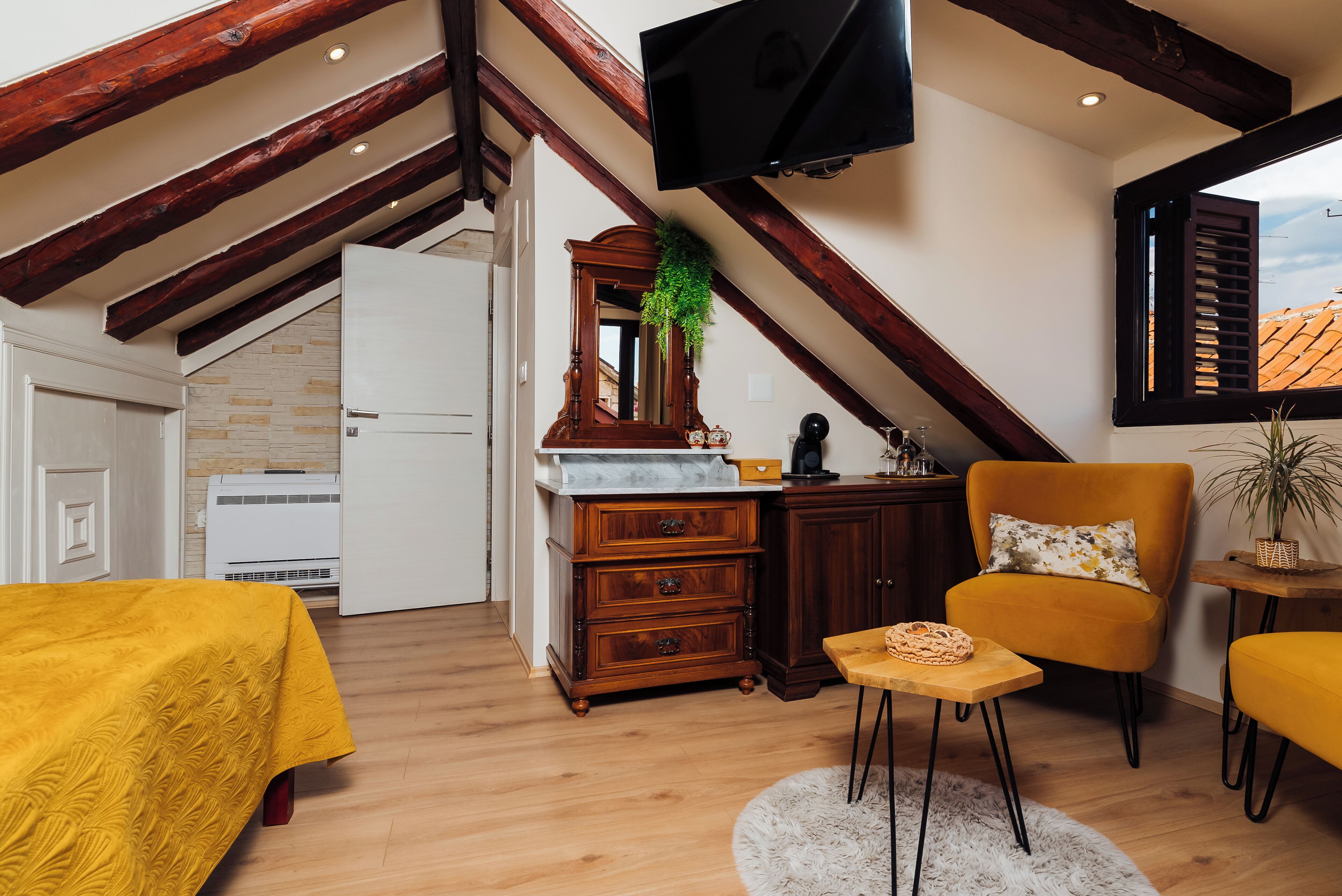 A cozy room with a wooden ceiling, a television, a yellow armchair, a small table, and a bed with a yellow bedspread.