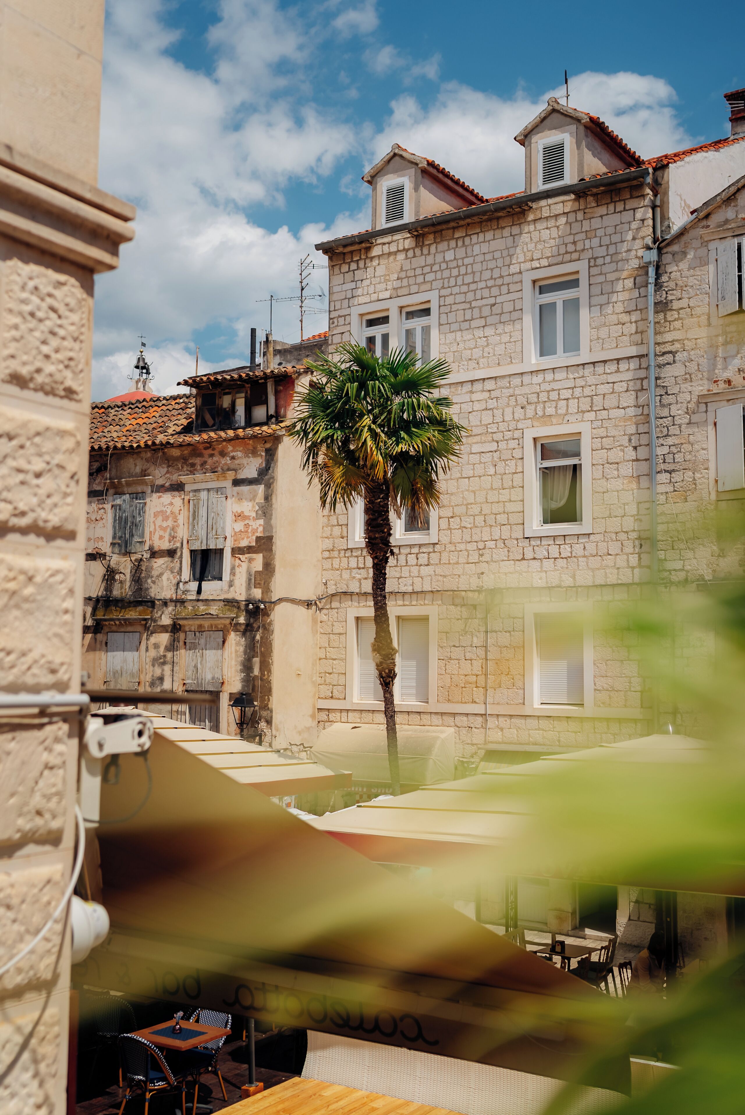 Un edificio con fachada de piedra, varias ventanas y una palmera frente a él.