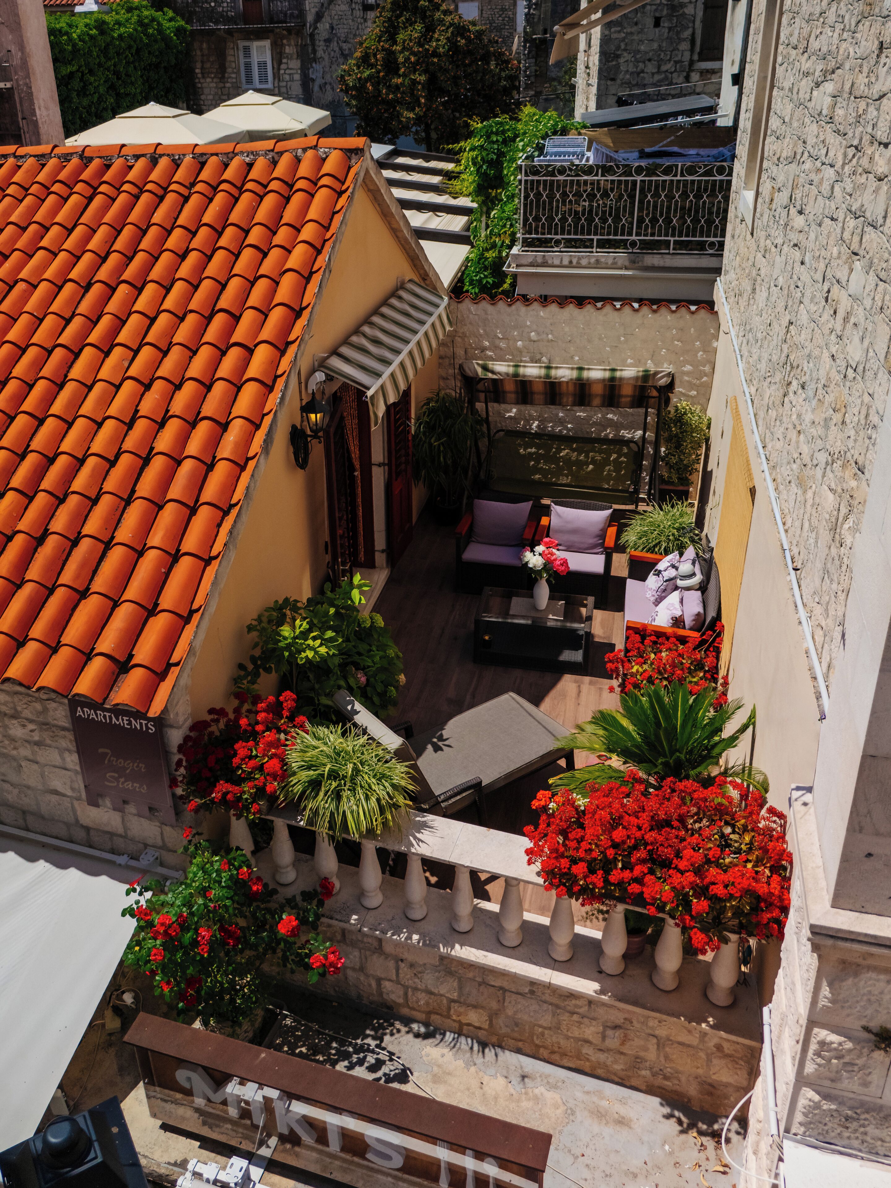 A courtyard with a tiled roof, a seating area with a bench and table, and potted plants with red flowers.