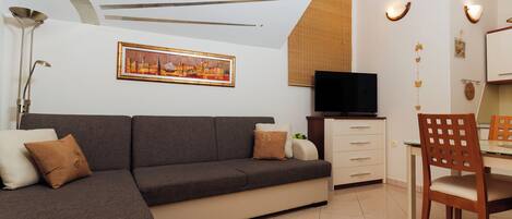 A modern living room with a sofa, a TV, a dining table, and a chair.