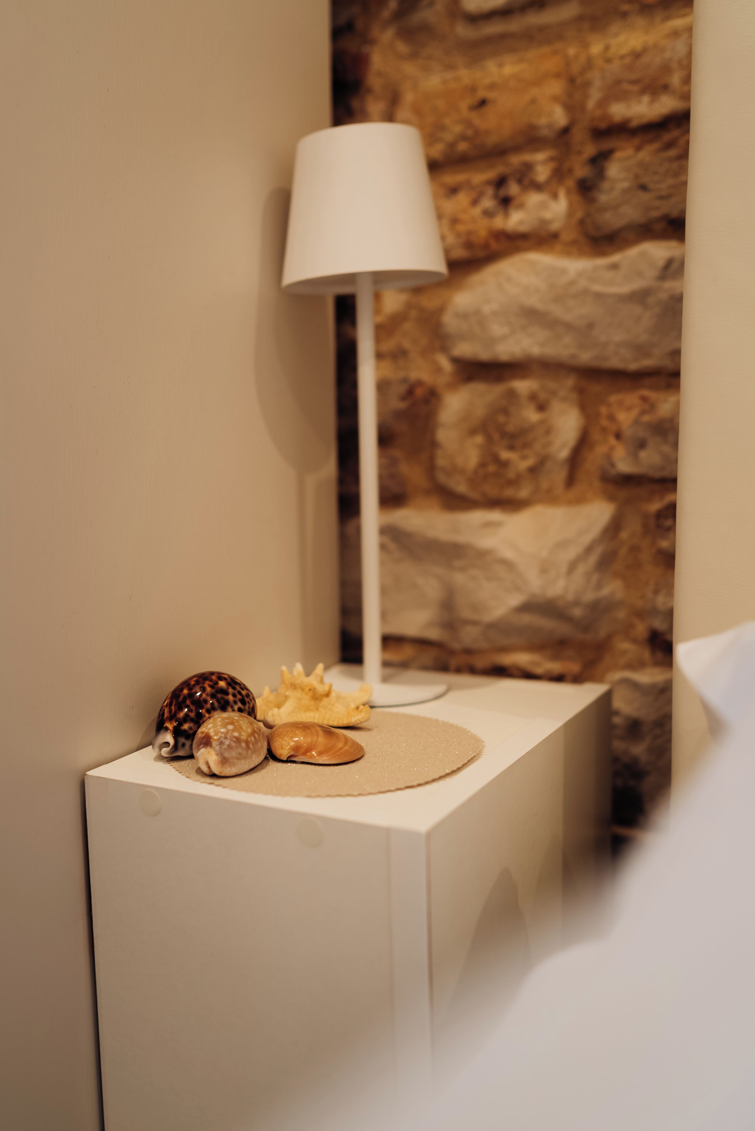 A bedside table with a lamp, decorative shells, and a stone wall background.