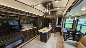 Cozinha moderna de RV com televisão de tela plana, micro-ondas, fogão e geladeira.