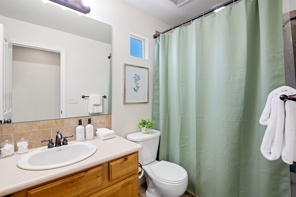 A bathroom with a sink, mirror, toilet, and green shower curtain. - Stylish modern 3BR near Old Town, CSU, and local breweries (Fort Collins)