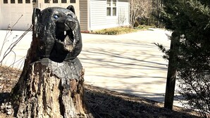 A house with a green roof and a tree stump sculpture in the front yard.
