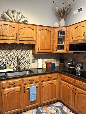 Una cocina con armarios de madera, encimera negra y salpicadero de azulejos.