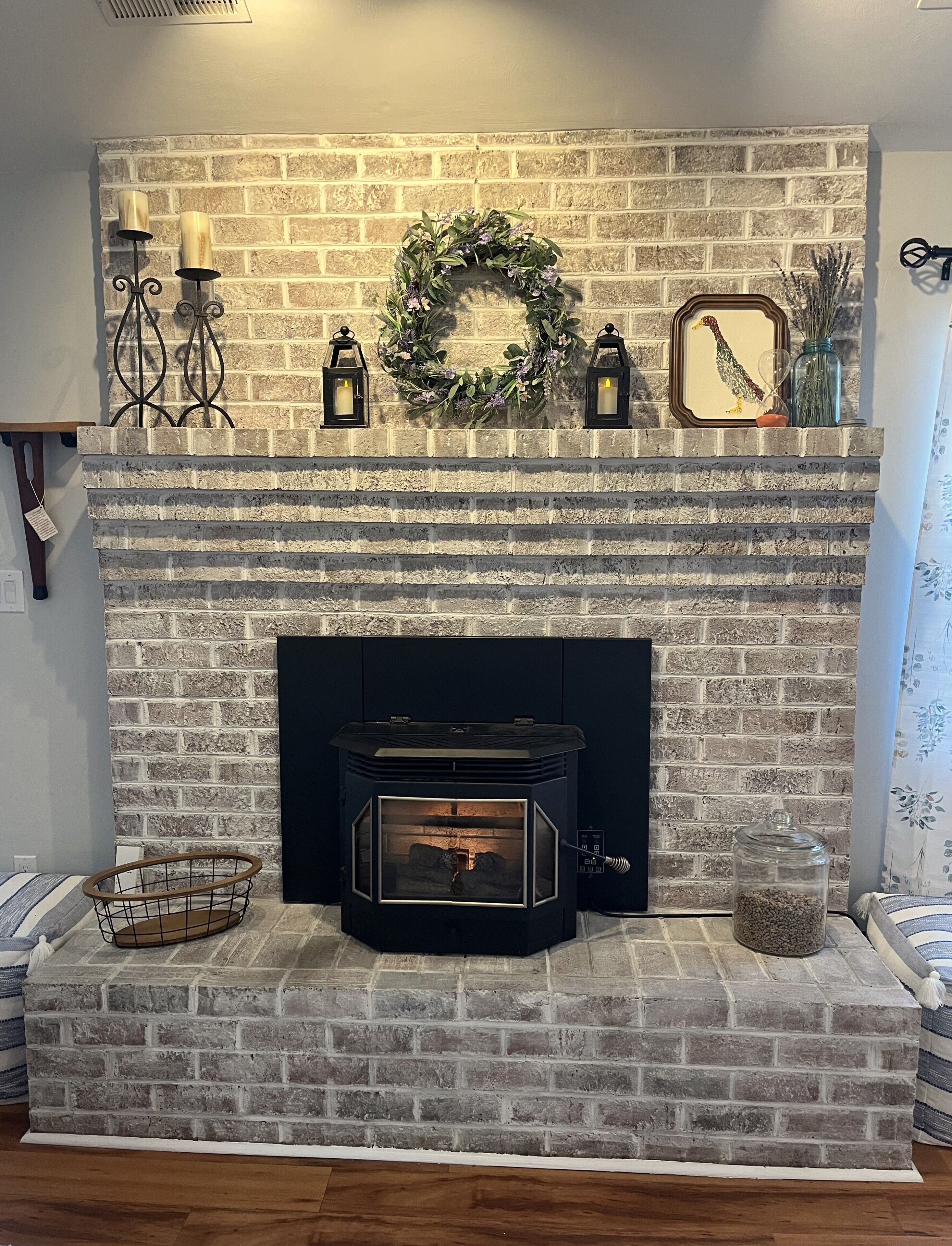 A fireplace with a brick wall, a decorative wreath, and two wall-mounted lanterns.