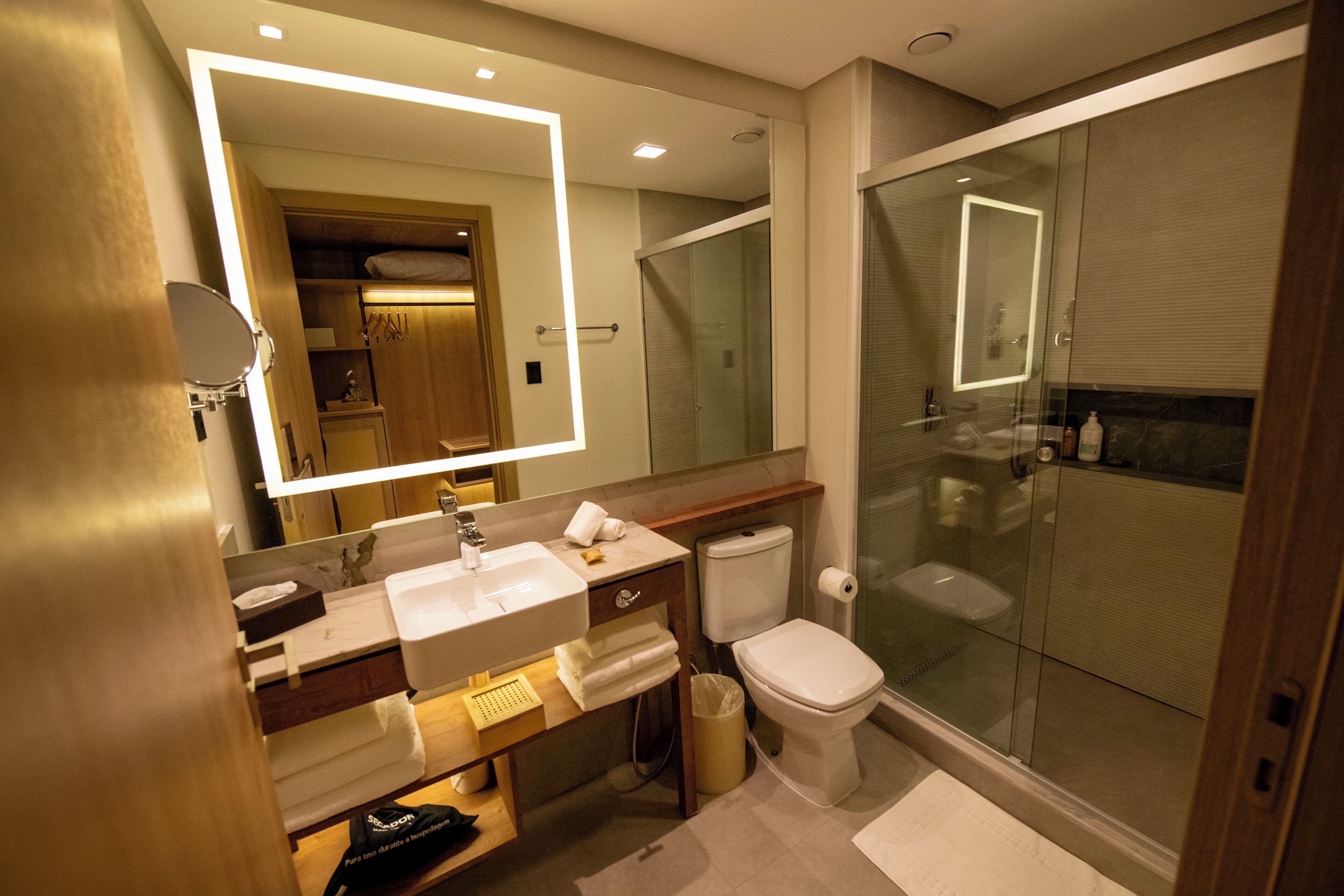 A modern bathroom with a large mirror, a glass-enclosed shower, and a white sink.