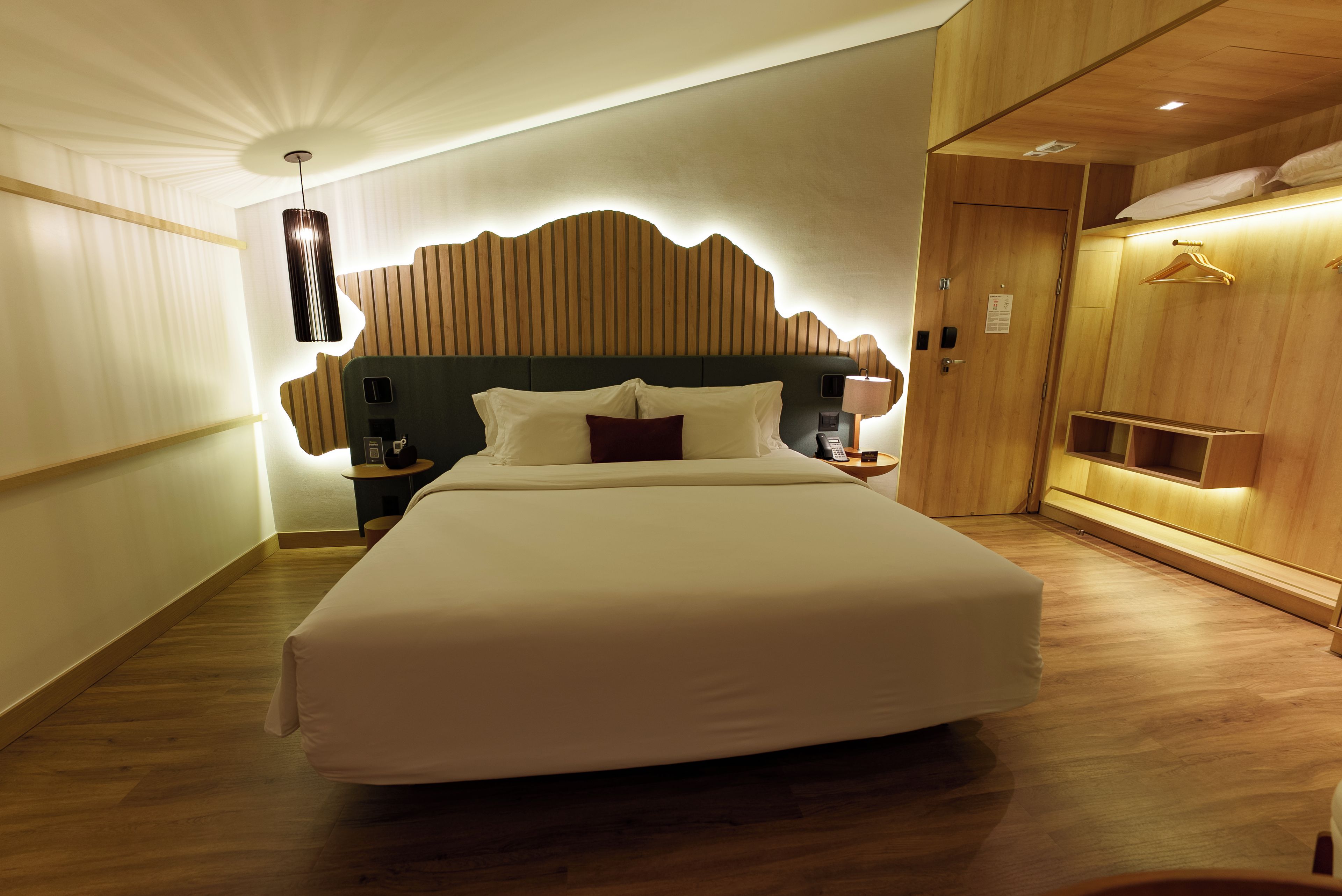 A hotel room with a large bed, a wooden headboard, a bedside table with a lamp, and a wardrobe.
