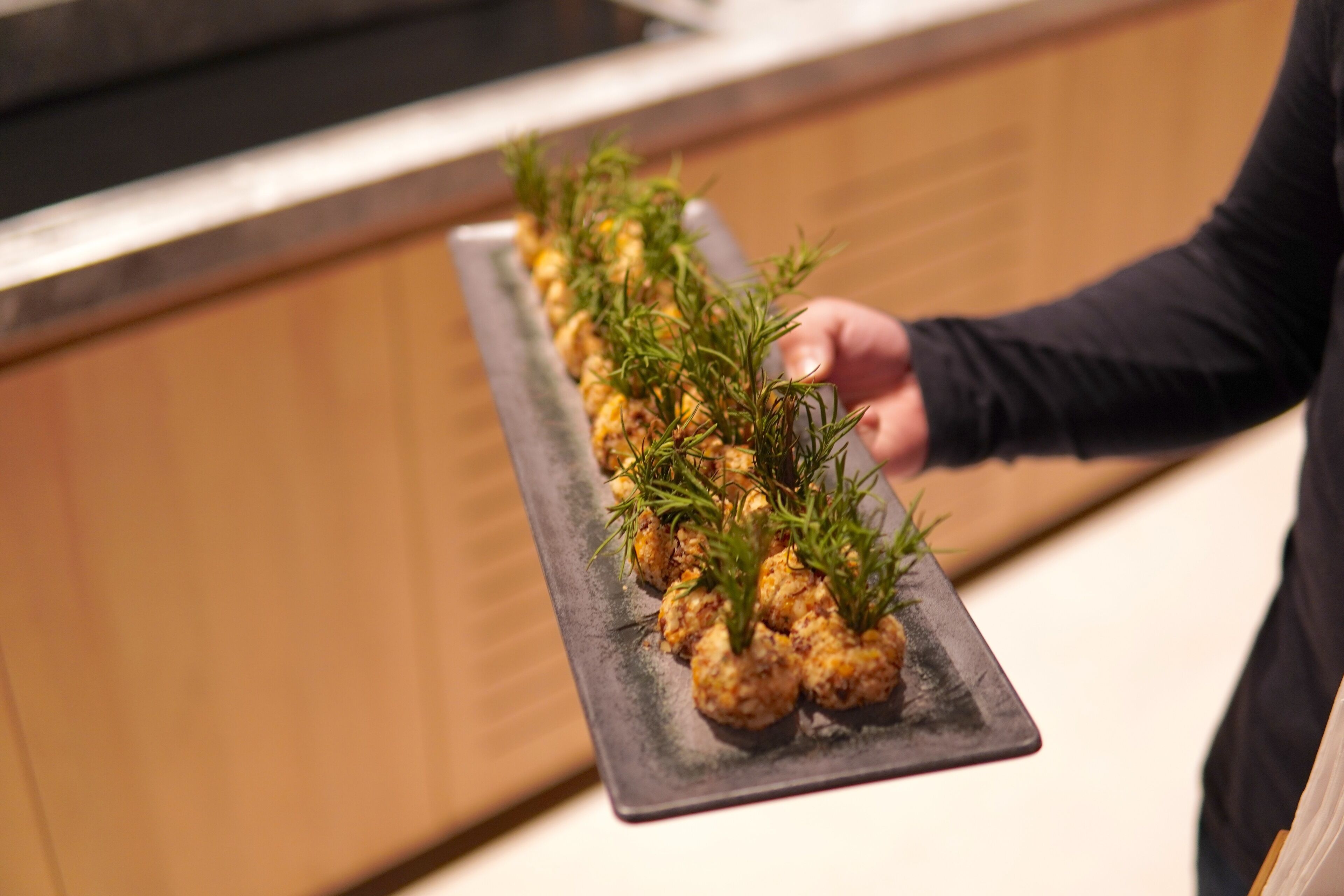 A person holding a rectangular black plate with food garnished with green herbs.