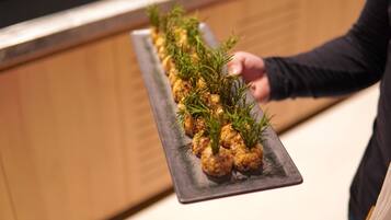 A person holding a rectangular black plate with food garnished with green herbs.